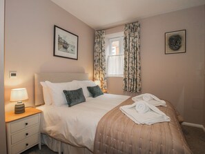 A neatly made bed with pillows, a bedside lamp, and a window with curtains. - The Old China Shop (Ludlow)