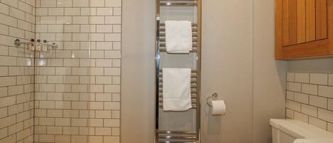 Un baño con pared de ducha azulejada, un toallero vertical, un inodoro y un armario de madera.