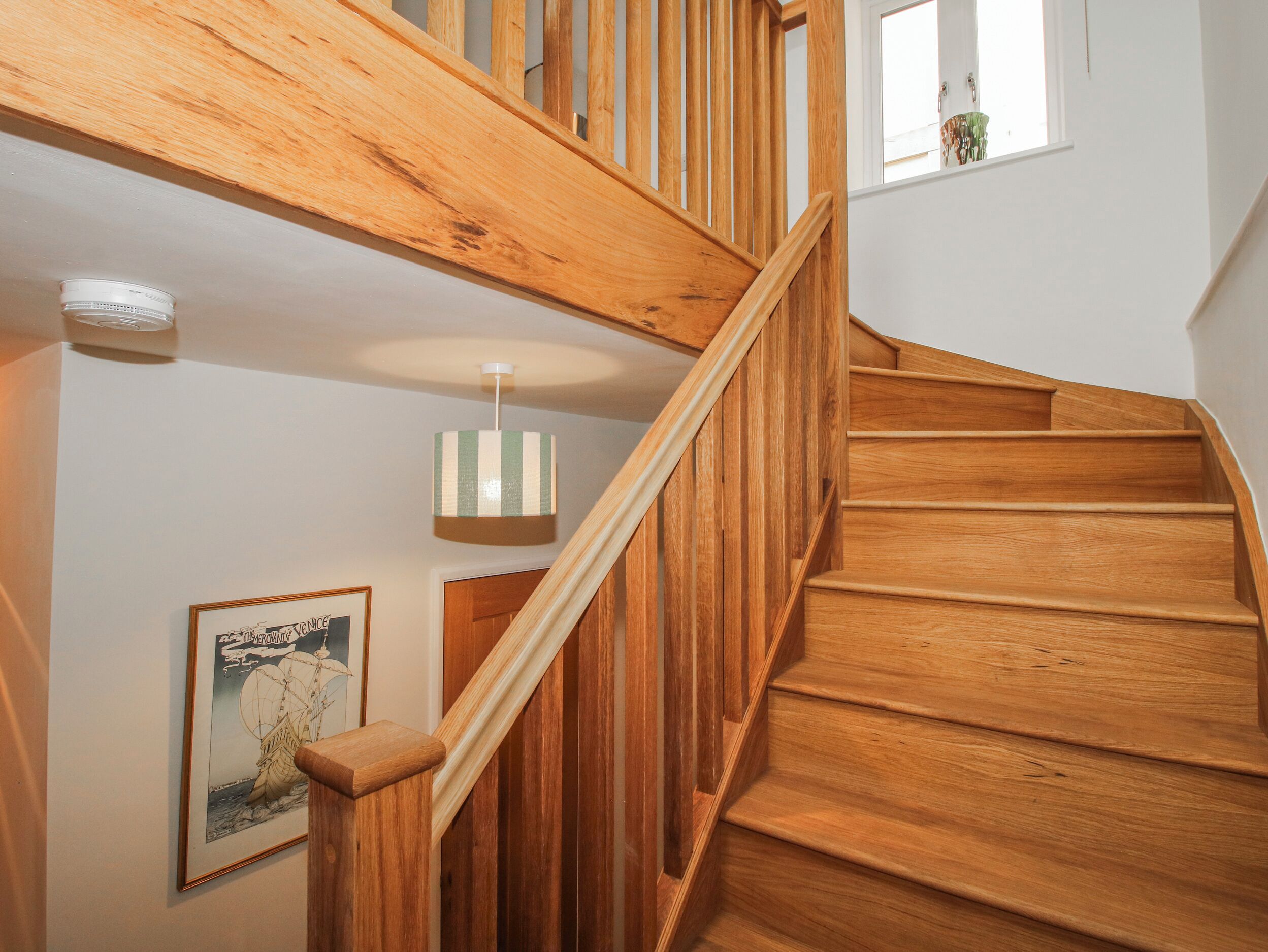 A wooden staircase with a handrail, a hanging light fixture, and a framed picture on the wall.