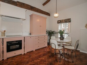 A kitchen with wooden herringbone flooring, a dining table with chairs, and a hanging light fixture. - The Old China Shop (Ludlow)