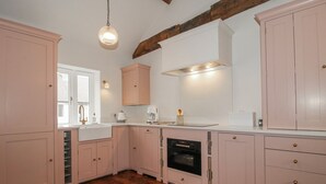 Ett kök med trägolv i fiskbensmönster, rosa skåp, en inbyggd ugn och en hängande lampa.