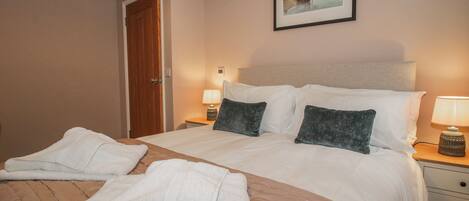 A hotel room with a bed, two pillows, a nightstand with a lamp, a framed picture on the wall, and a door.