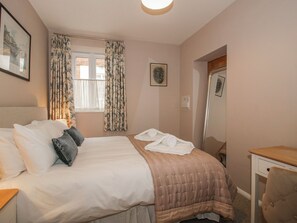 A bedroom with a bed, a desk, a chair, a window with curtains, and a framed picture on the wall. - The Old China Shop (Ludlow)
