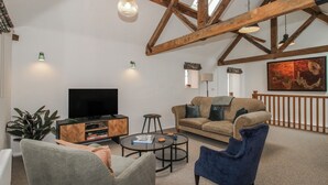 Ett vardagsrum med en TV, en soffa, stolar, ett soffbord och en tavla på väggen.