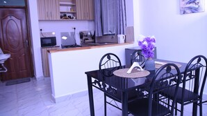 Une cuisine compacte équipée d’un four à micro-ondes, d’une cuisinière et d’un évier, un coin repas avec une table et des chaises, et une porte donnant sur une autre pièce.