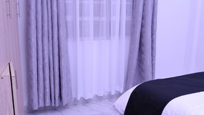 Une chambre à coucher avec un lit, une armoire, un tapis moelleux et une fenêtre avec des rideaux légers.