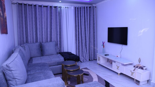 Un salon moderne avec un canapé d’angle, un téléviseur et une console blanche.