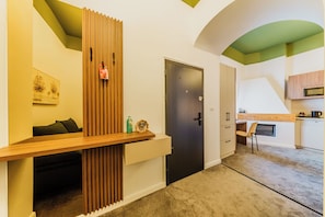 A modern interior with a wooden accent wall, a dark door, a kitchen area with a microwave, and a seating area with a sofa.