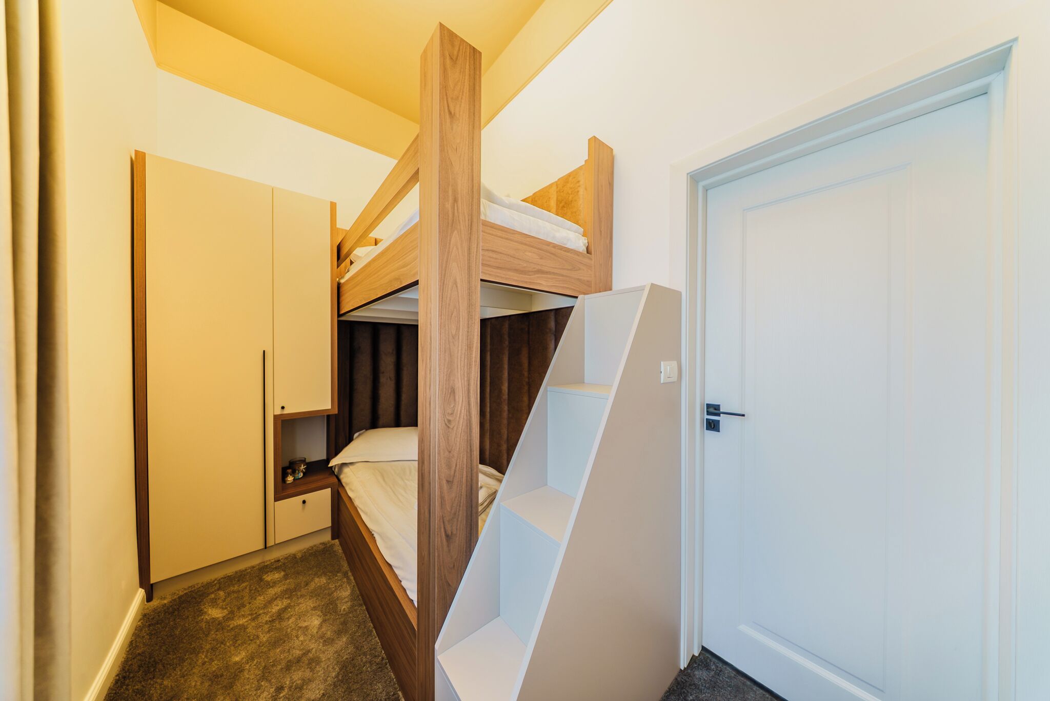 A bunk bed with a wooden frame, a white door, and a built-in desk with a chair.