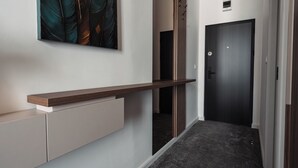 A hallway with a dark door, a light-colored wall, and a wooden shelf.