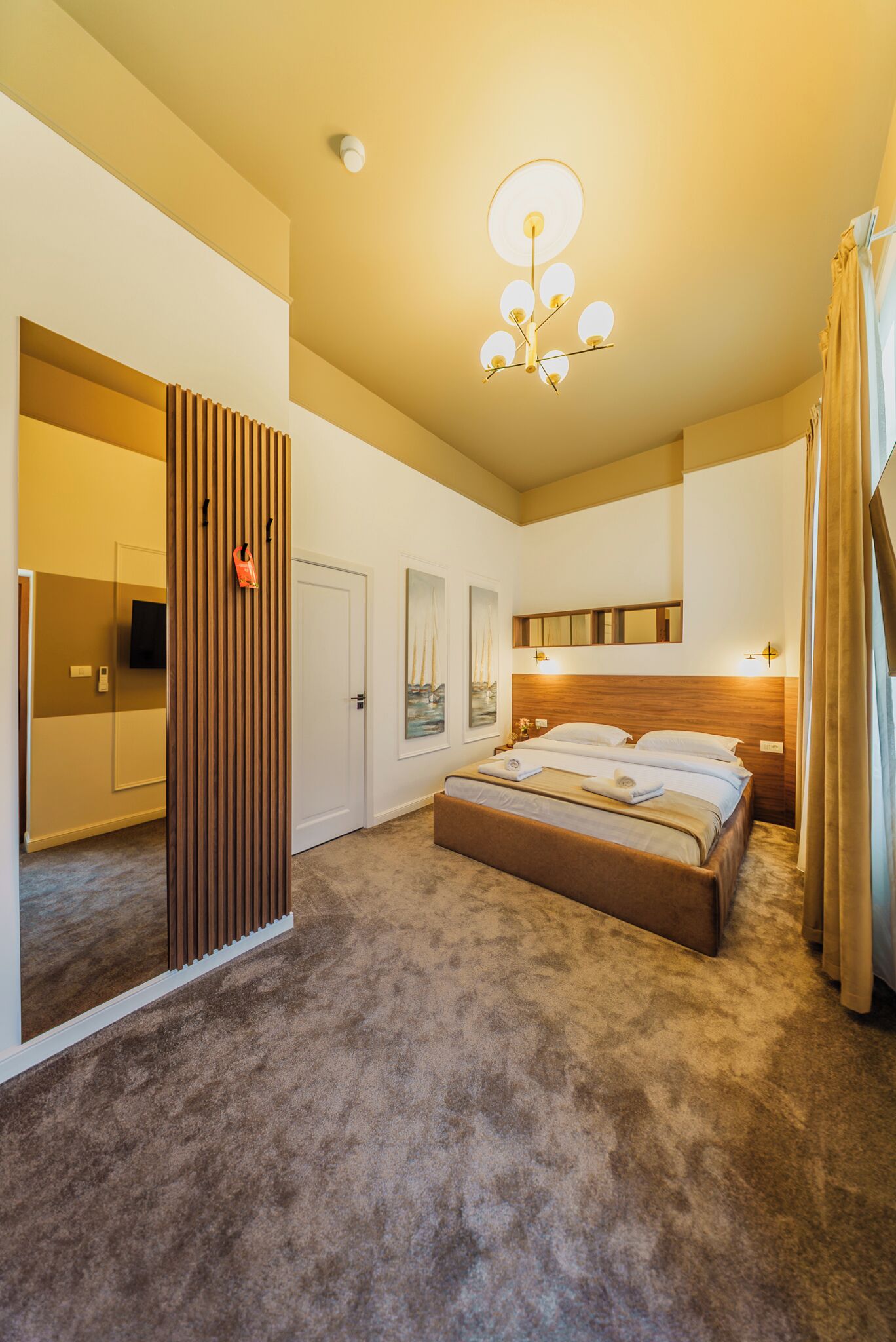 A hotel room with a large bed, a wooden partition, a flat-screen TV, and a ceiling light fixture.