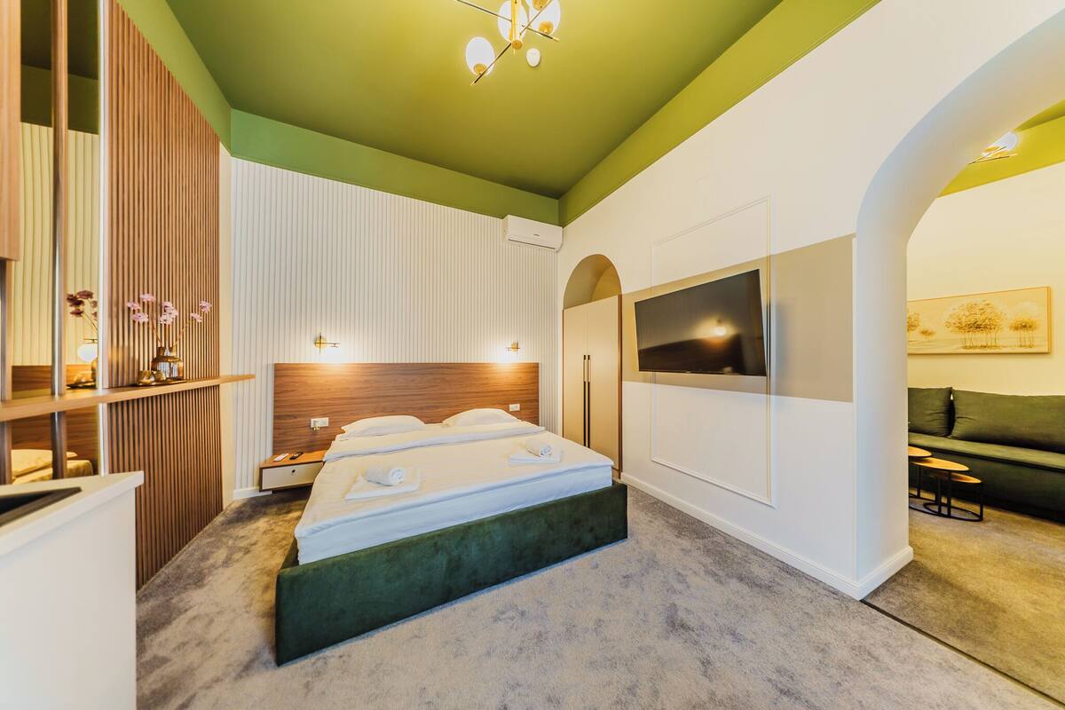 A modern bedroom with a large bed, a TV, and a green accent wall.