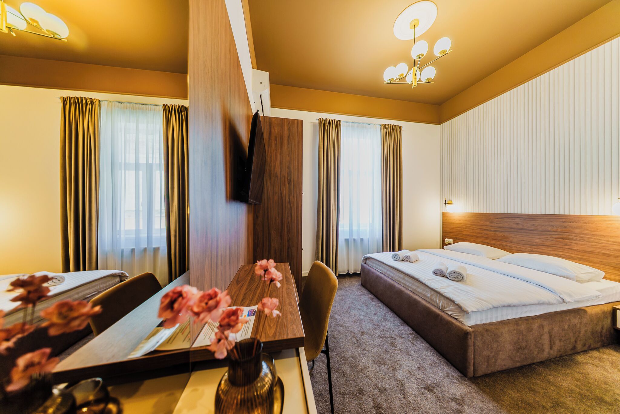 A hotel room with a bed, a desk with a chair, a vase with flowers, and curtains.