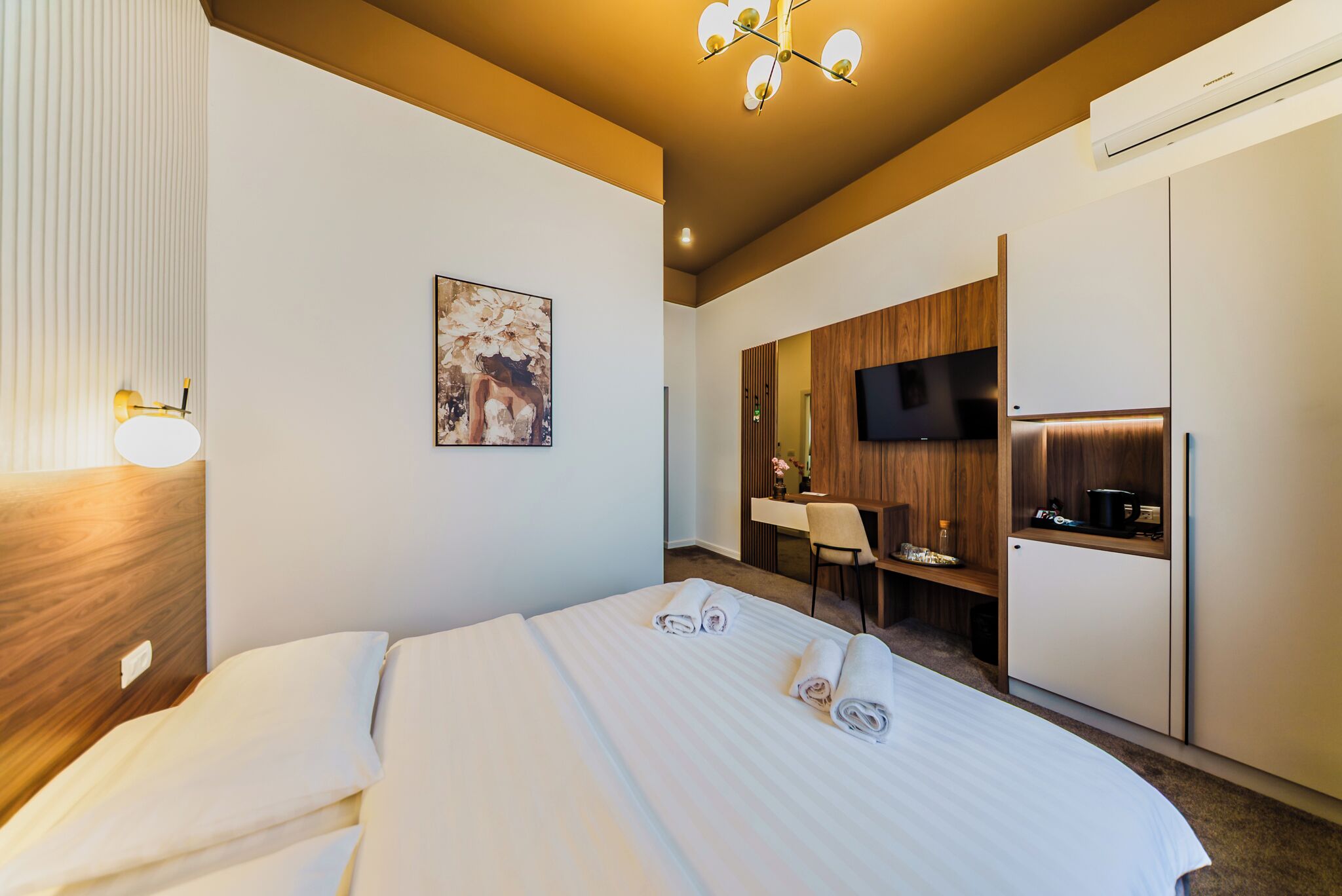 A hotel room with a bed, a desk, a TV, and a kitchenette.