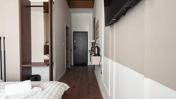 A narrow hallway with a bed on the left, a door at the end, and a mounted TV on the right wall.