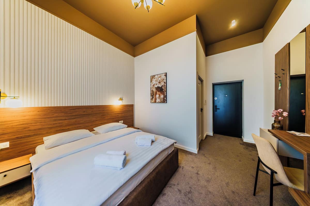 A hotel room with a large bed, bedside tables, a desk, and a mirror.
