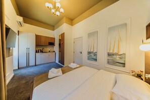 A hotel room with a bed, a kitchenette, and two sailboat paintings on the wall.