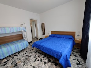A room with a bunk bed, a single bed, a mirror, a desk with a lamp, and a door leading to another room. - Seafront Property Near Caorle Historic Center (Caorle)