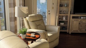 A living room with a beige sofa, a table with a lamp and a plant, a TV stand with a flat-screen TV, and a door leading to a balcony. - Spacious 2-bedroom condo at Sea Oats -D206 in beautiful Gulf Shores, Alabama (Gulf Shores)