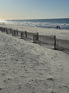 A sandy beach with a wooden fence, ocean waves, and two people in the distance. - Spacious 2-bedroom condo at Sea Oats -D206 in beautiful Gulf Shores, Alabama (Gulf Shores)