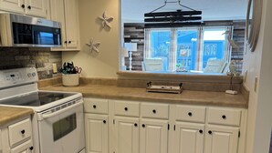 A kitchen with white cabinets, a microwave, stove, and a window with a view. - Spacious 2-bedroom condo at Sea Oats -D206 in beautiful Gulf Shores, Alabama (Gulf Shores)