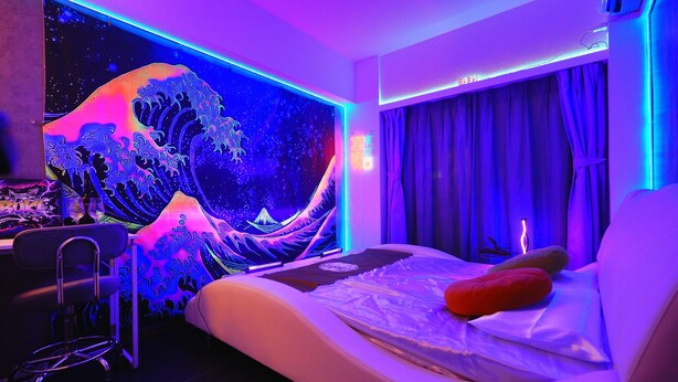 A modern bedroom with a bed, a chair, a wall with a wave pattern, and a digital clock. - 4 min to Shinjuku central/Comfortable bed/Cyber Shinjuku Room (新宿区余丁町)
