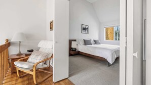 Een slaapkamer met een bed, een stoel, een nachtkastje, een lamp en een foto aan de muur.