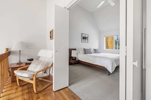 A bedroom with a bed, a chair, a nightstand, a lamp, and a picture on the wall.