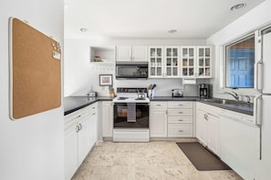 Una cocina con armarios blancos, microondas, estufa y fregadero.