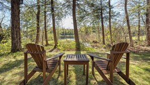 Een picknickopstelling met twee houten stoelen en een tafel, gelegen in een bosrijk gebied met een meer op de achtergrond.