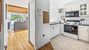 Een moderne keuken met witte kasten, een magnetron, fornuis en een prikbord aan de muur.