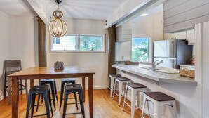 Una cocina con una mesa de madera, taburetes de bar, una lámpara colgante y un ventanal.