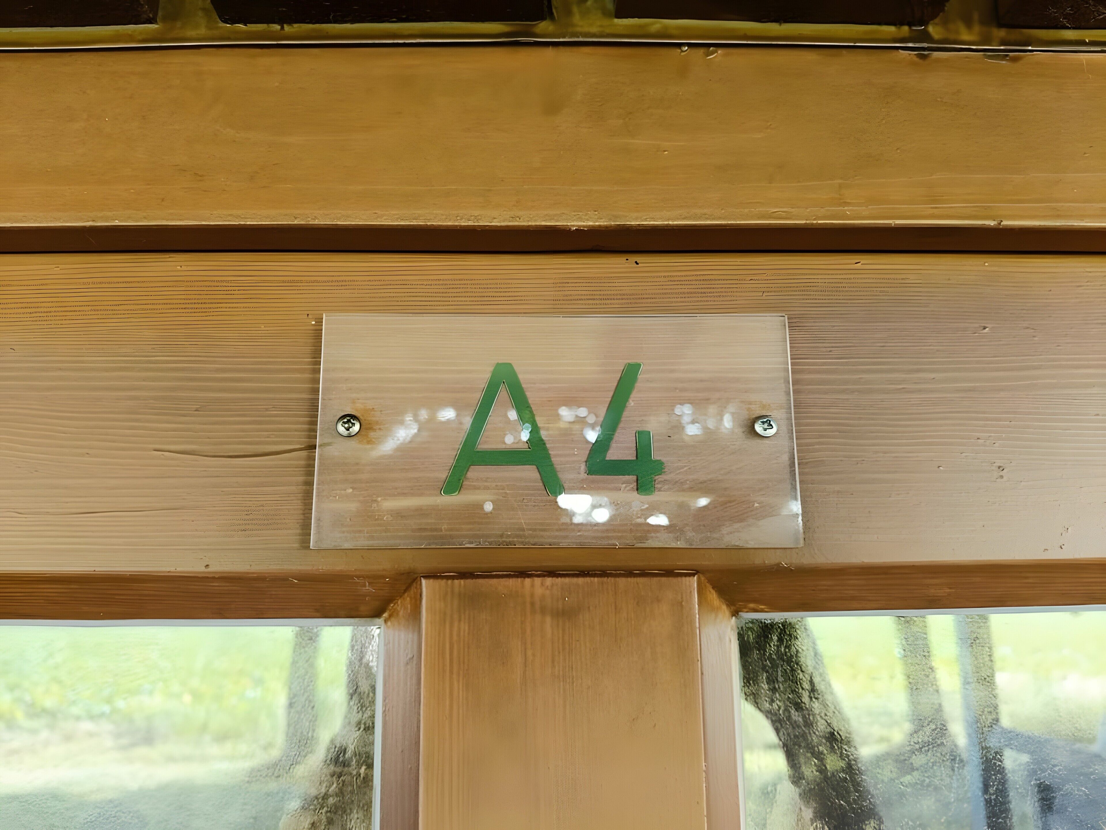 Eine Holztür mit einer Metallschildern, auf der 'A4' steht, und zwei sichtbaren Schrauben.