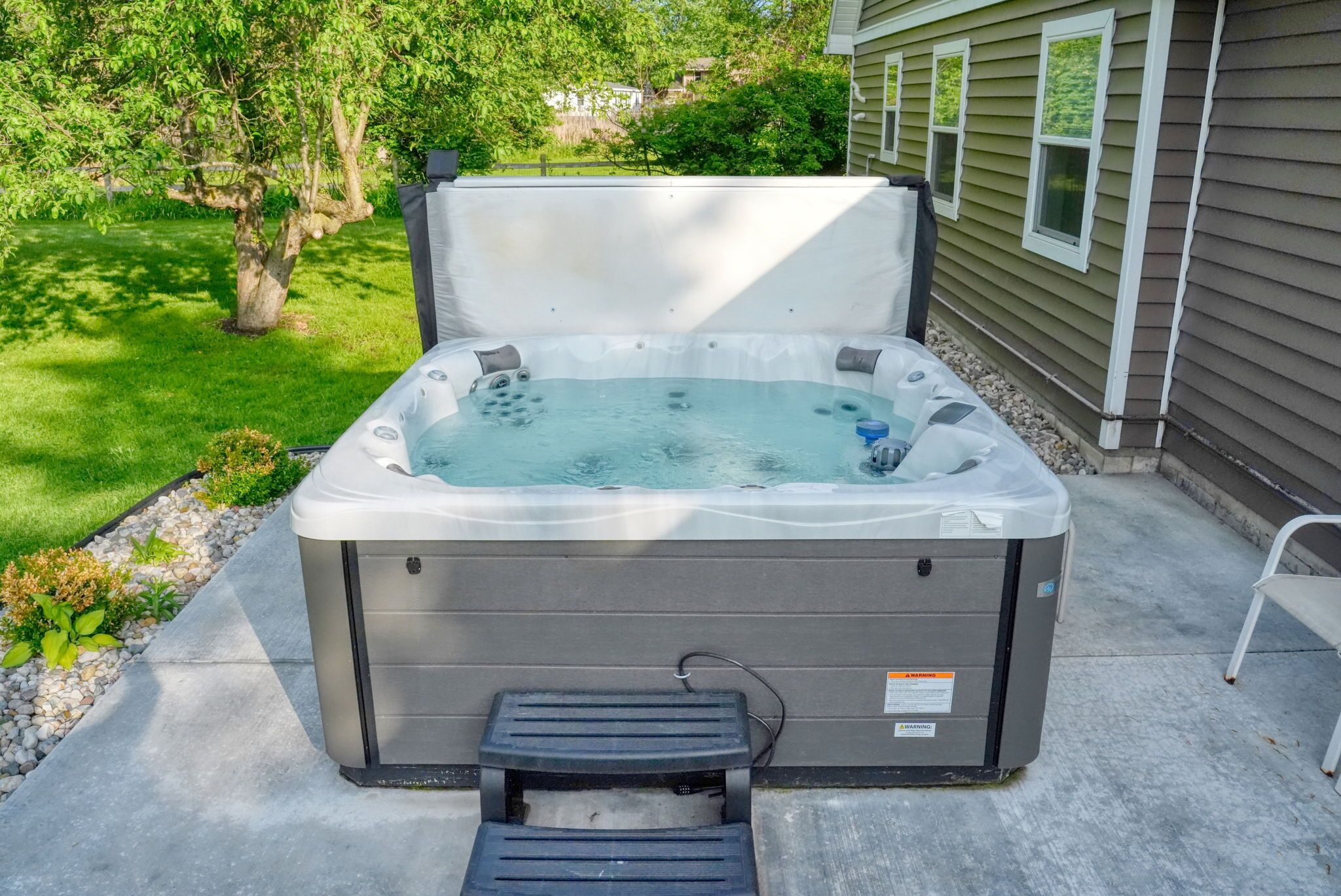 A hot tub with a step, set on a concrete patio with a house in the background.