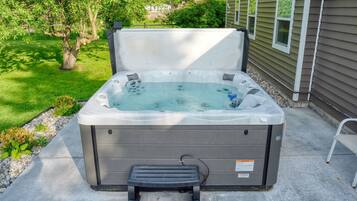A hot tub with a step, set on a concrete patio with a house in the background.