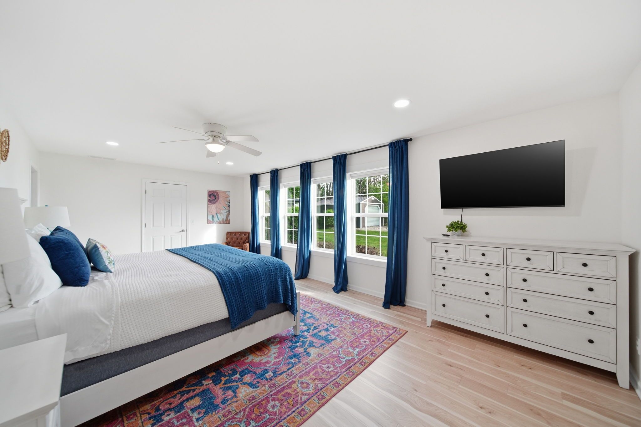A bedroom with a bed, a dresser, a TV, and a window with curtains.