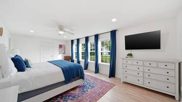 A bedroom with a bed, a dresser, a TV, and a window with curtains.
