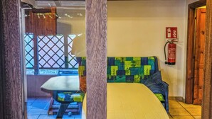 A room with a white table and a colorful sofa, a fire extinguisher on the wall, and a wooden ceiling. - Alloggio privato AS (San Teodoro)