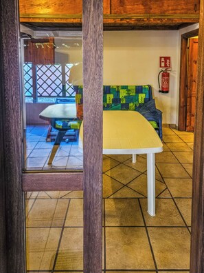 A room with a white table and a colorful sofa, a fire extinguisher on the wall, and a wooden ceiling. - Alloggio privato AS (San Teodoro)