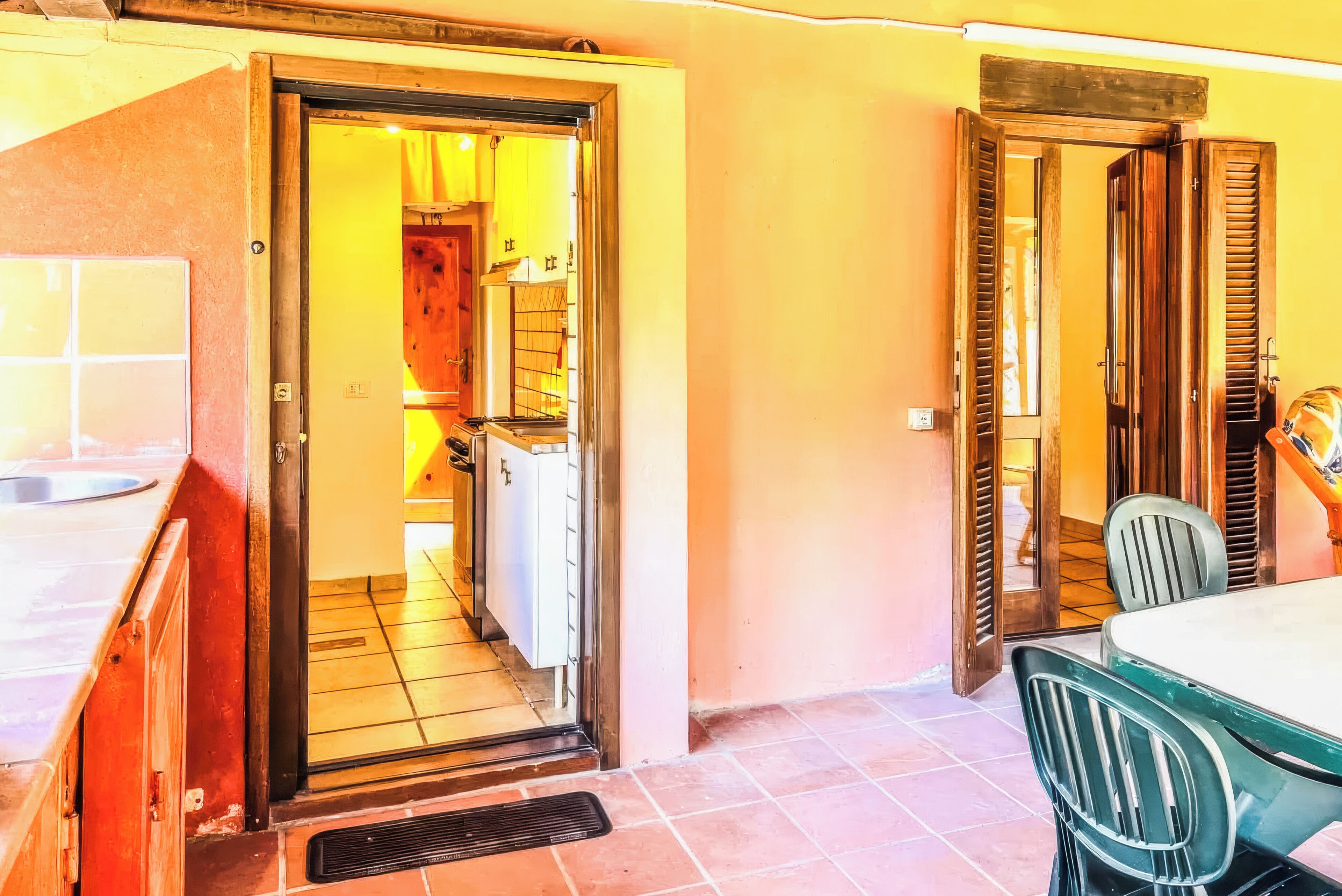 A room with a tiled floor, a sink, a window, and a door leading to another room.