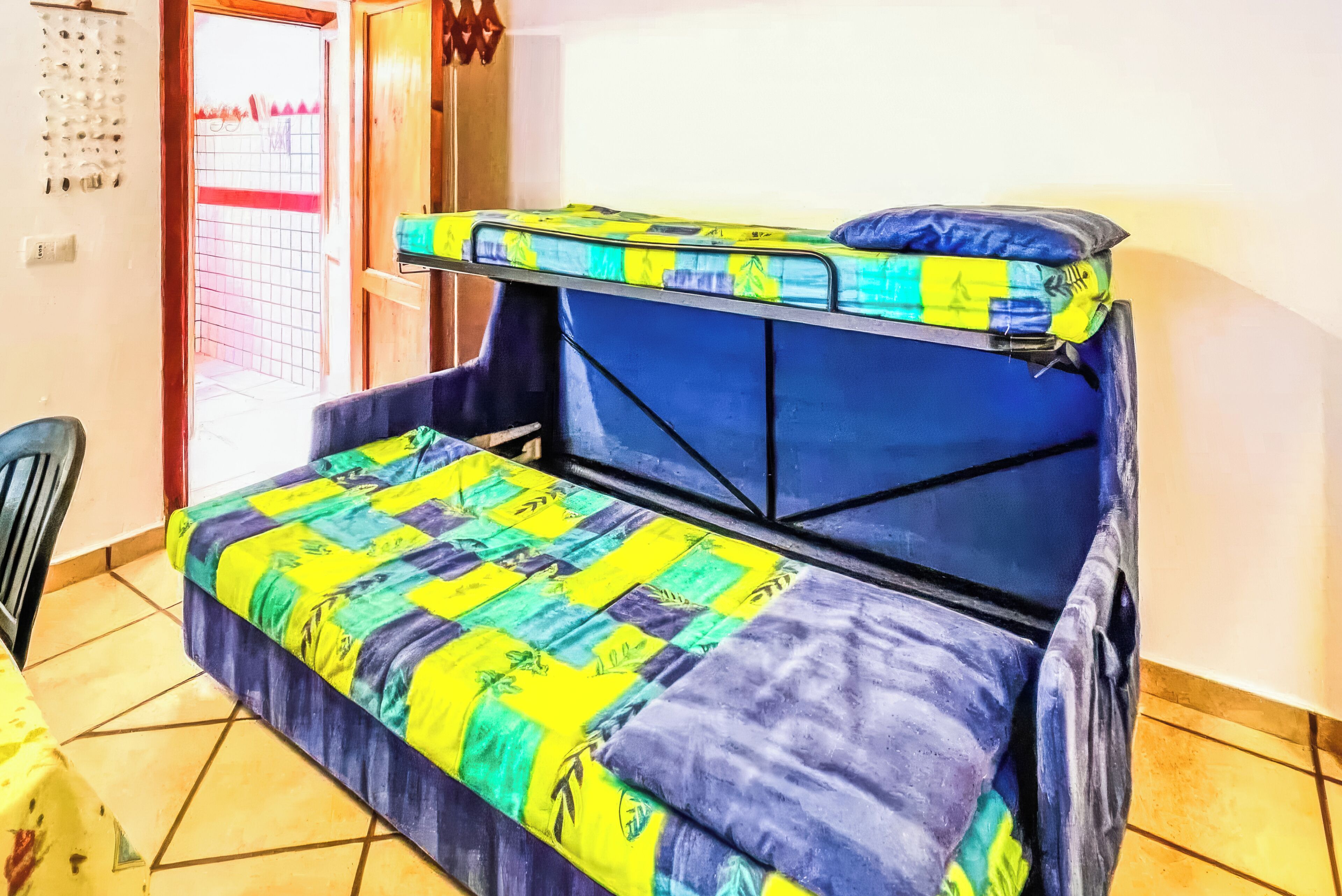 A room with a bunk bed, a chair, and a door with a metal gate.