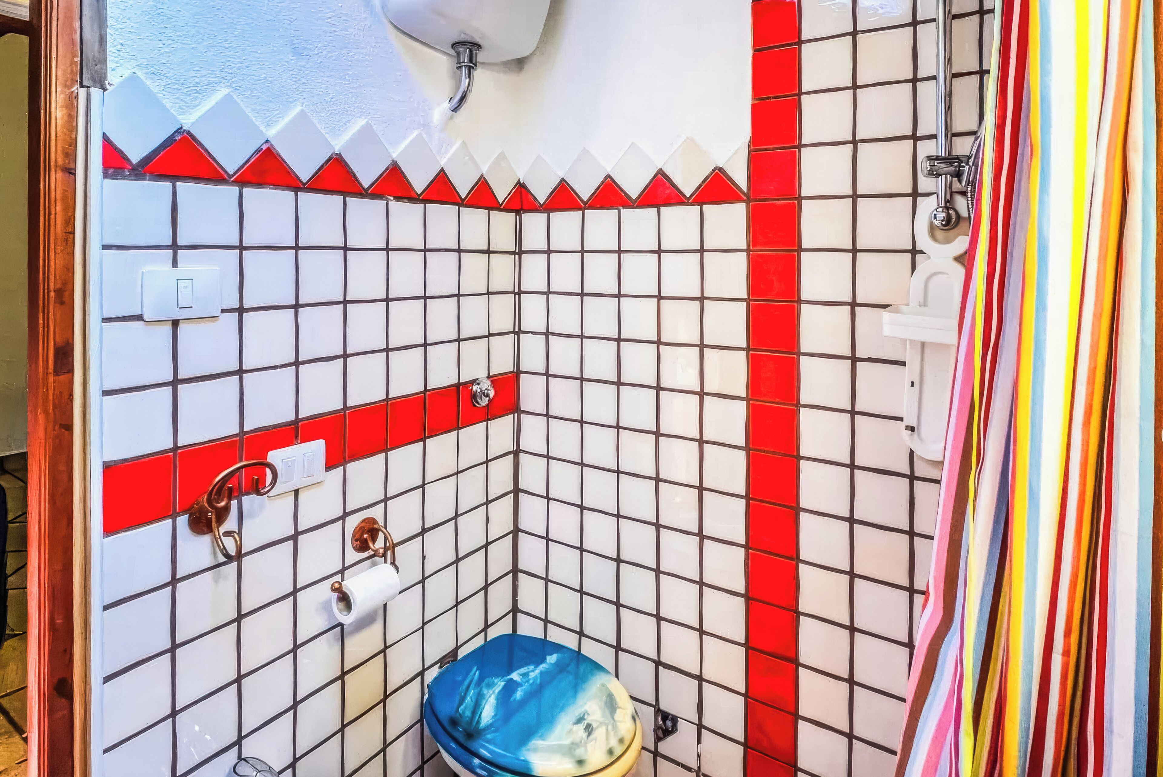 Een badkamer met wandtegels in het wit en rood, een blauw toilet en een douchegordijn.