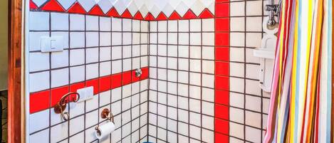 Een badkamer met wandtegels in het wit en rood, een blauw toilet en een douchegordijn.