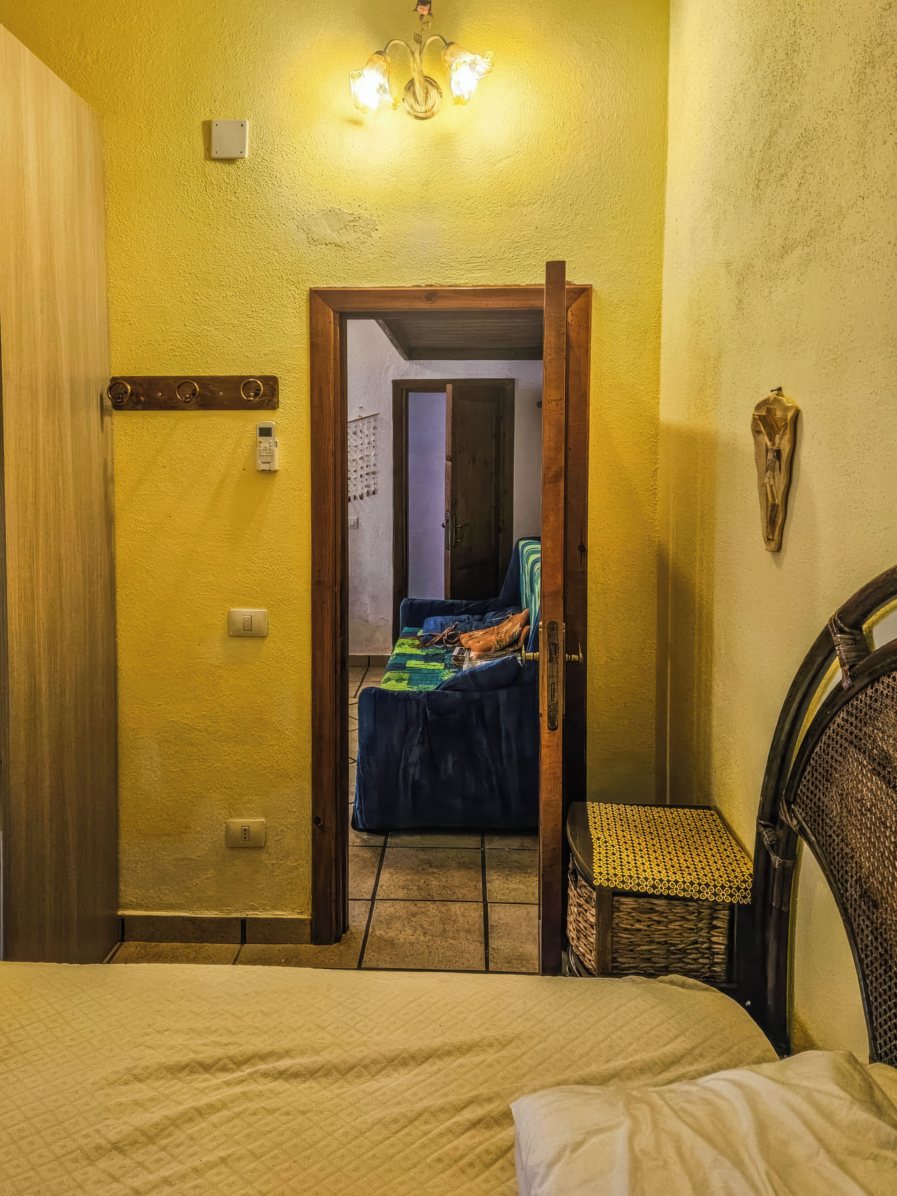 A bedroom with a bed, a chair, a door leading to another room, and a wall-mounted light fixture.