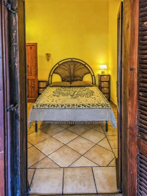 A bed with a headboard, a bedside table with a lamp, and a wooden door frame. - Alloggio privato AS (San Teodoro)