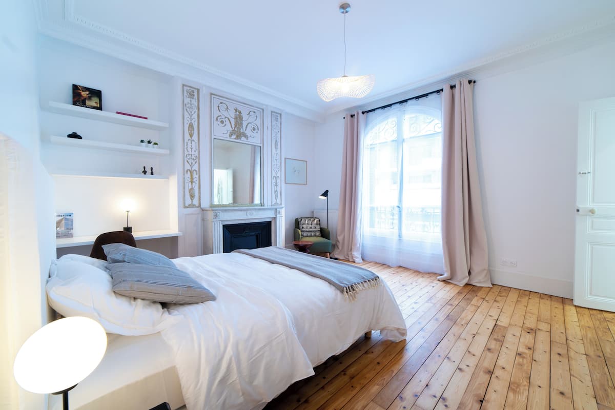 A bedroom with a bed, a fireplace, a mirror, and a window with curtains.