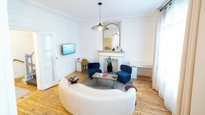 A living room with a white sofa, two blue armchairs, a coffee table, a fireplace, and a large mirror. - Finestate Coliving Dupleix (Paris)
