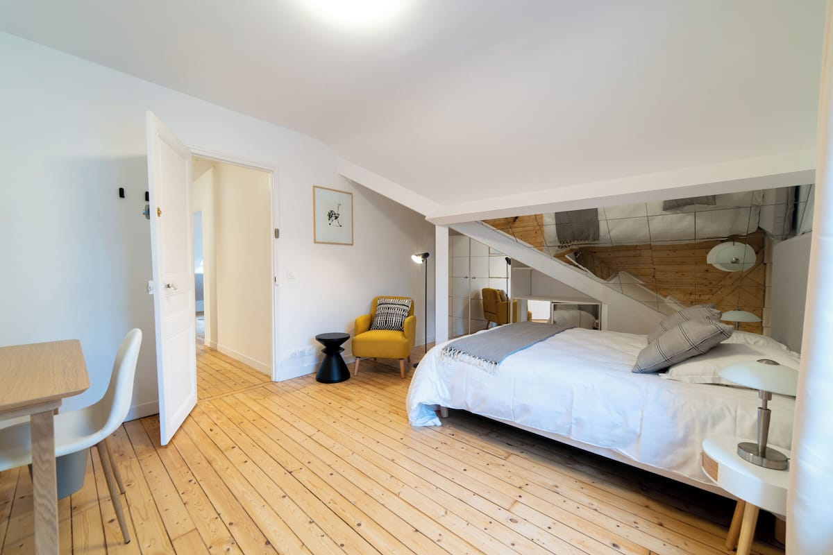 A bedroom with a bed, a desk, a chair, and a staircase.