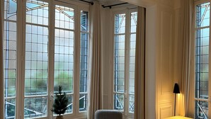 A room with large windows, a chair, a small table, and a lamp. - Finestate Coliving Dupleix (Paris)