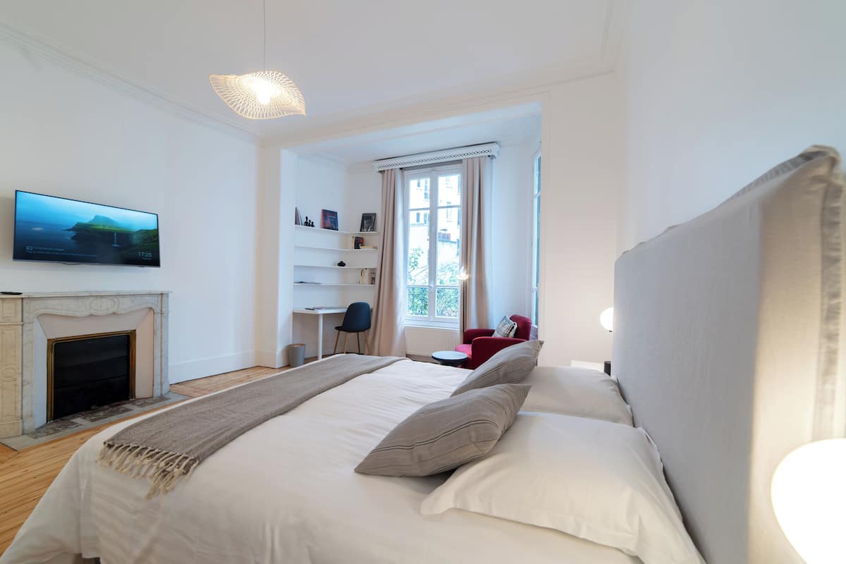 A bedroom with a bed, a television, a fireplace, a desk, and a window with curtains.